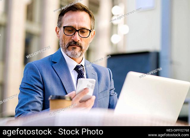 Mature businessman using smart phone sitting in cafe