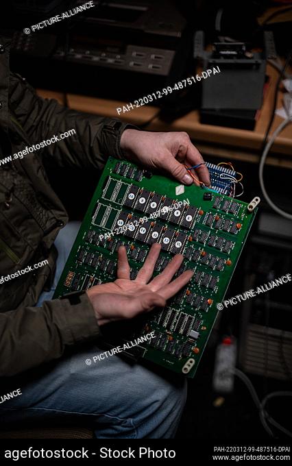 PRODUCTION - 05 March 2022, Hessen, Seligenstadt: Employee Simon holds a circuit board of an arcade game at the Pinball and Arcade Museum