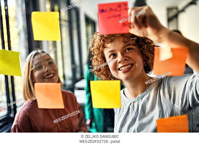 Happy colleagues with sticky notes at glass pane in office
