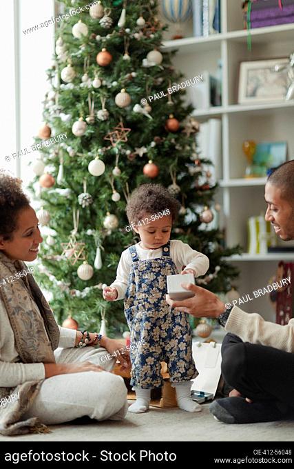 Couple helping baby daughter open Christmas gift in living room