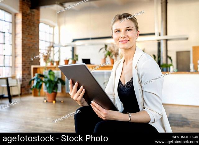 Smiling young businesswoman with tablet pc sitting in living room at home
