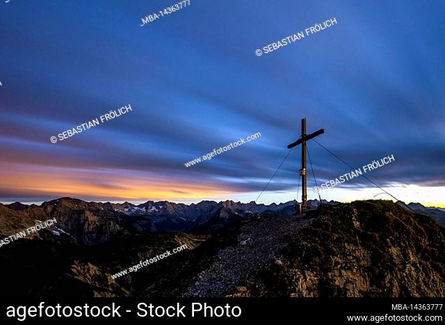 The summit cross of the Mondscheinspitze in the Karwendel, shortly after sunset. Through the long exposure, the colors of the night show and the clouds blur