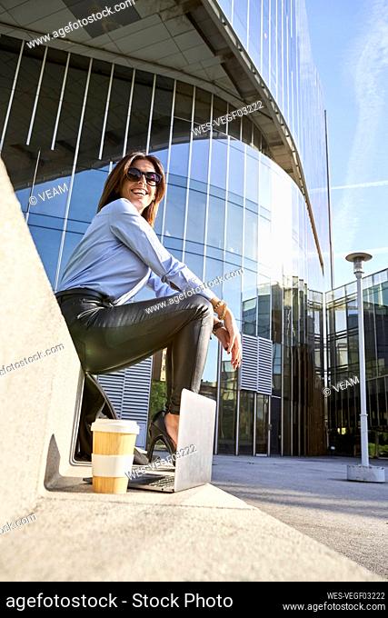 Smiling businesswoman sitting on bench by office building