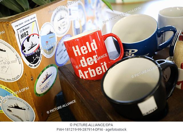 19 December 2018, Hamburg: Coffee cups, one with the inscription ""Held der Arbeit"", are standing in a holder on the bridge of the research vessel ""Meteor""...