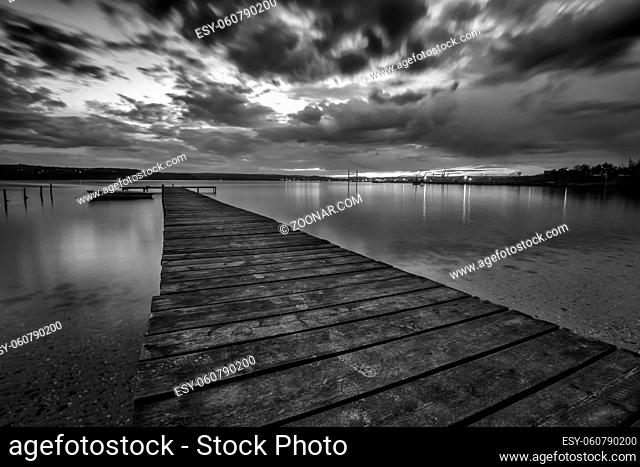 Black and white landscape with wooden pier and fishing boat at the lake after sunset