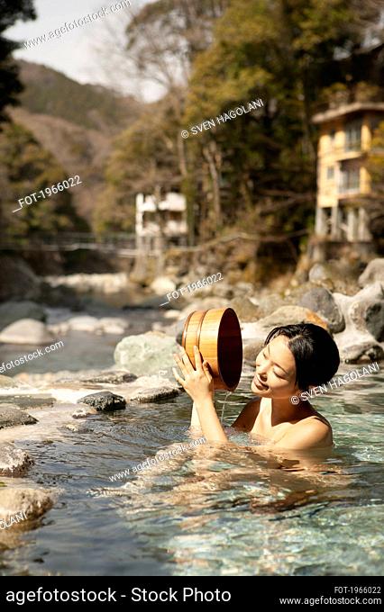 Happy young woman with bucket in sunny pool at Onsen, Izu, Japan
