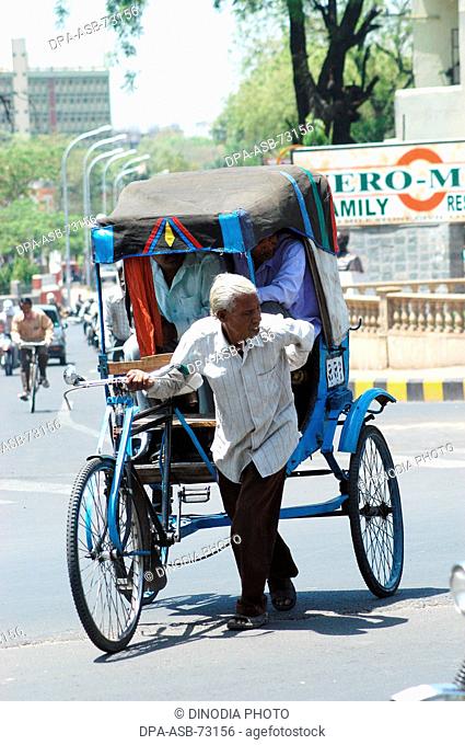 A old cycle rickshaw puller carrying passengers at Nagpur , Maharashtra , India
