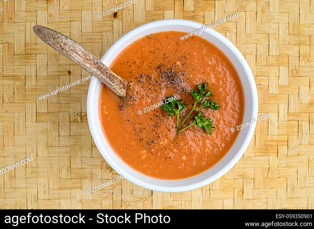 A studio overview photo of a bowl of tomato soup with a sprig of parsley on top