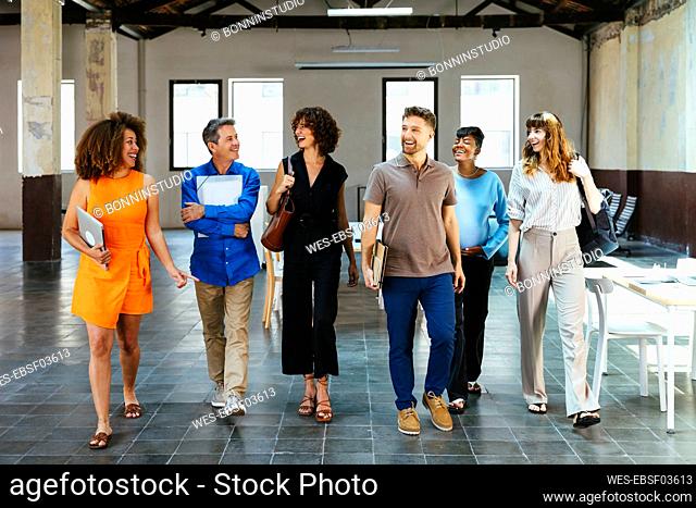Happy businesswomen and businessmen walking together in office