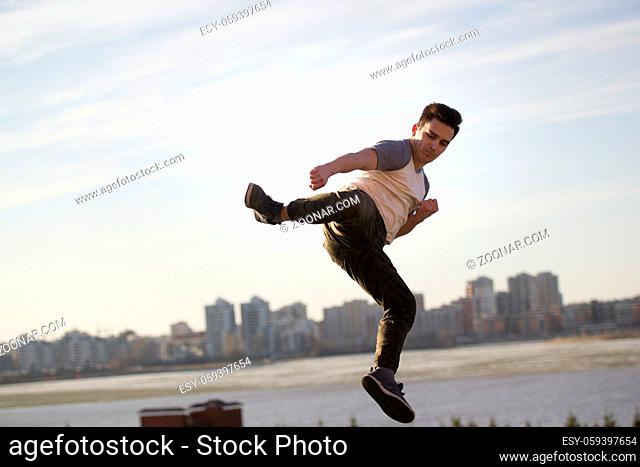 Young man fighter performs acrobatic kick in front of skylineYoung male kick fighter performs acrobatic kick in front of skylinetelephoto shot