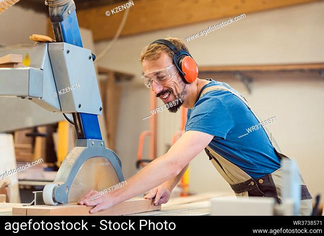 Diligent carpenter with fun at work sawing piece of wood