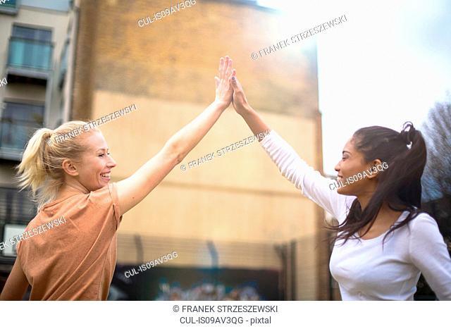 Two young women giving high five, outdoors