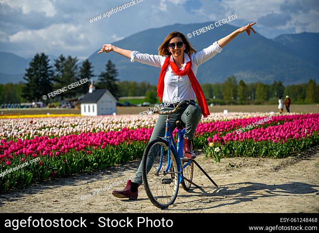 Very happy, very excited caucasian woman sitting on her old bike by the tulip field. Arms and legs wide open and she shows happiness in British Columbia, Canada