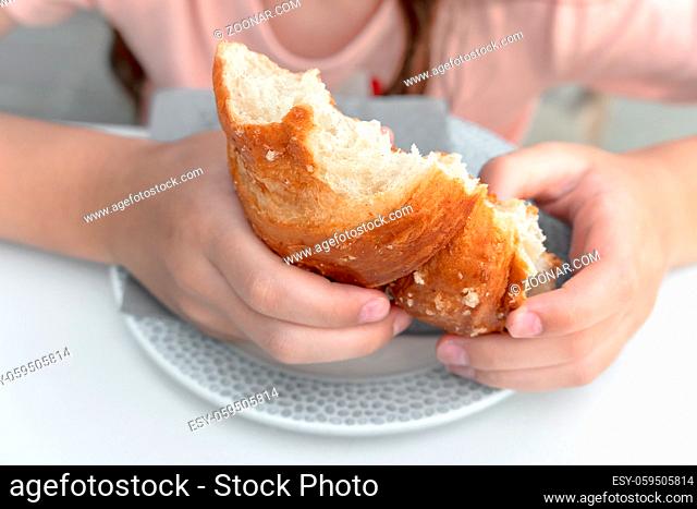 Pretty little girl eats a fresh croissant for breakfast. Portrait of cute girl with yummy face enjoy eating croissant. Healthy food for children concept
