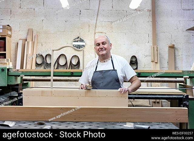 Smiling mature man holding plank while standing at workshop