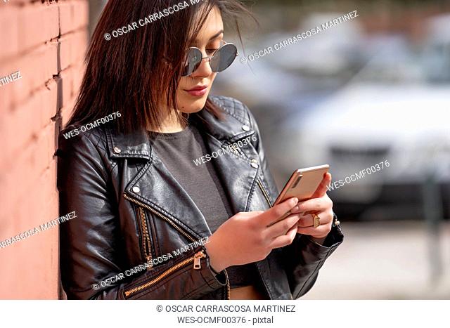Portrait of young woman wearing sunglasses and black leather jacket looking at smartphone