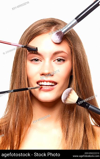 beautiful young woman getting natural make up. makeup brushes against face. studio beauty shot isolated on white background. copy space
