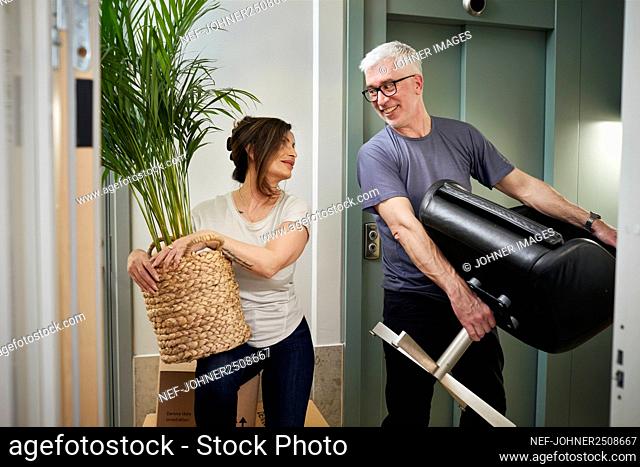 Mature couple carrying plant and chair