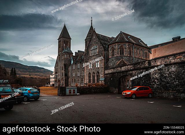 FORT AUGUSTUS, SCOTLAND, DECEMBER 17, 2018: The Abbey Highland Club, full of mold and lichen in its stone walls, under heavy cloudscape with mountains in the...