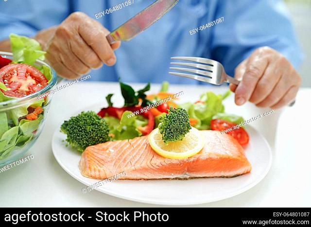 Asian elderly woman patient eating salmon stake and vegetable salad for healthy food in hospital