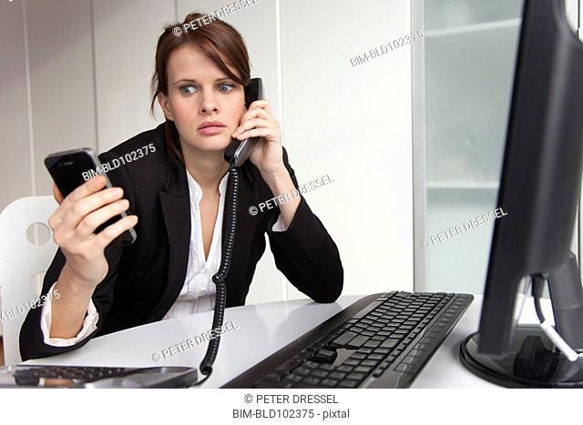 Businesswoman holding cell phone and talking on landline phone