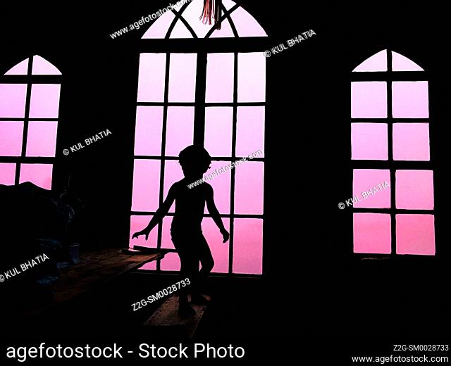 A young kid standing in a sporting posture in an attic with glass windows, Nova Scotia, Canada