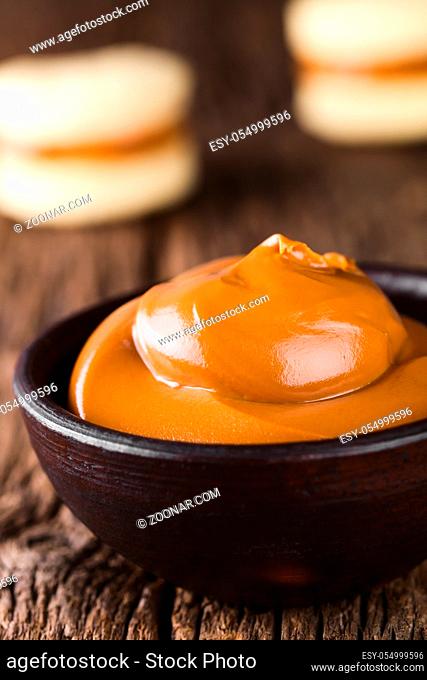 Latin American sweet caramel-like Manjar or Dulce de leche used as spread or filling in baking, photographed in small bowl with alfajor cookies in the back...