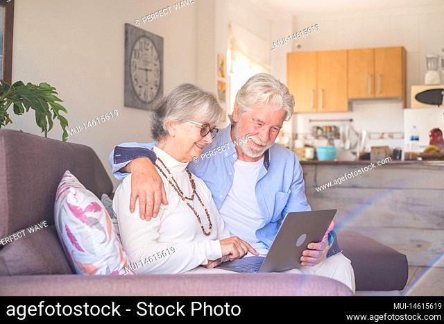 Couple of two old and mature people at home using tablet together in sofa. Senior use laptop having fun and enjoying looking at it