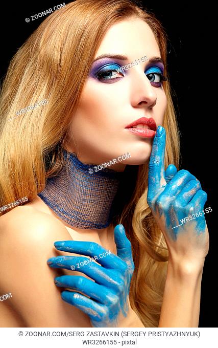 Young blonde woman with long hair and hands painted in blue paint with finger on lips