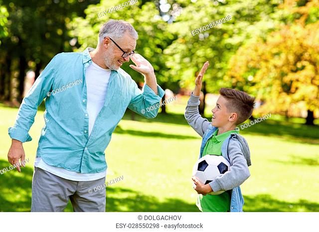 family, generation, gesture, sport and people concept - happy grandfather and grandson with football ball making high five at at summer park