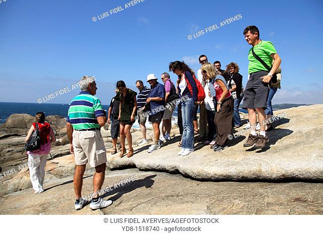 Tourists leaping over a stone in front of the shrine to da Barca, Muxía, A Coruña, Galicia, Spain