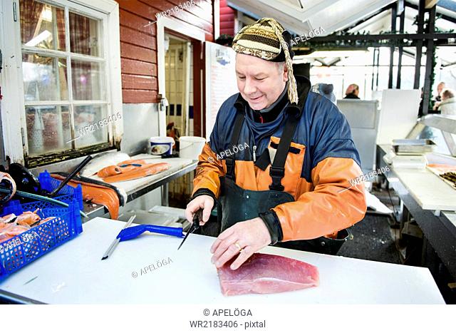 Happy mature fisherman filleting salmon in fishing industry