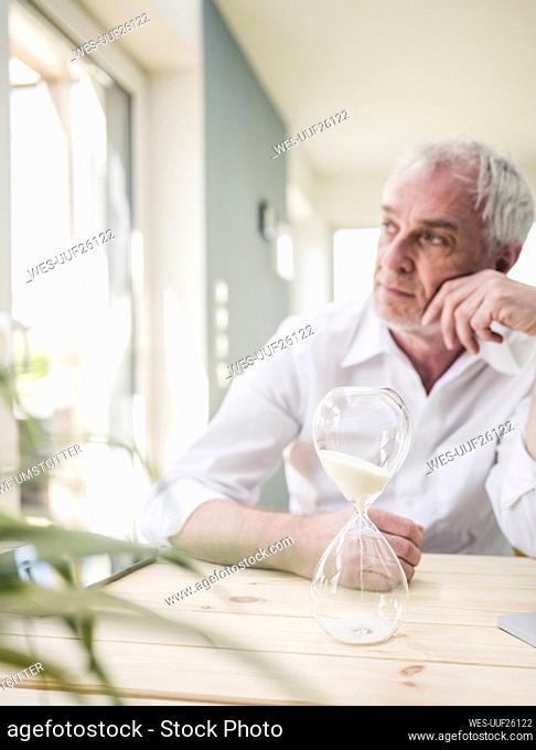 Hourglass on table with thoughtful senior man sitting in background