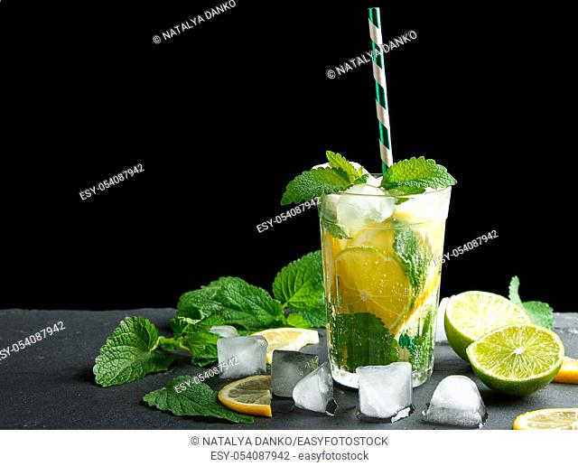 summer refreshing drink lemonade with lemons, mint leaves, ice cubes and lime in a glass on a black background, copy space