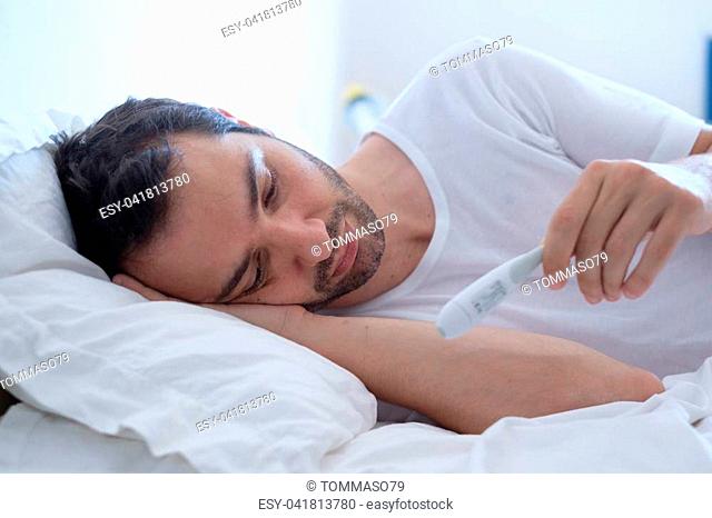 Sick man in bed measuring temperature feeling fever