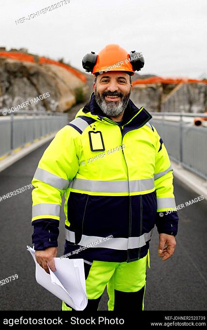 Portrait of male engineer in reflecting clothing standing on bridge