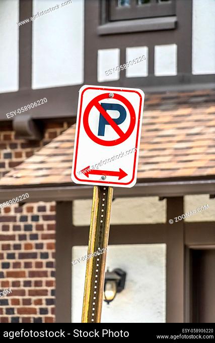 Close up view of a No Parking sign against a building on a sunny day. The red arrow indicates that parking is prohibited on both sides of the sign