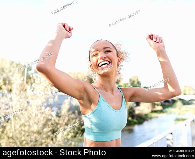 Cheerful athlete enjoying with arms raised under sky