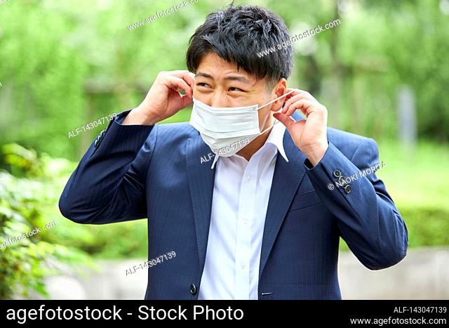 Young Japanese businessman wearing mask in the hot Summer downtown Tokyo