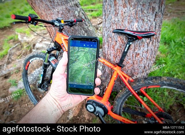 cyclist with e-bike consults the map of an app on a smartphone during an excursion through dirt paths in the dolomites, belluno, veneto, italy