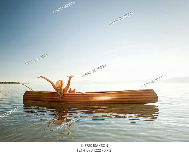 Young woman relaxing in canoe with arms raised