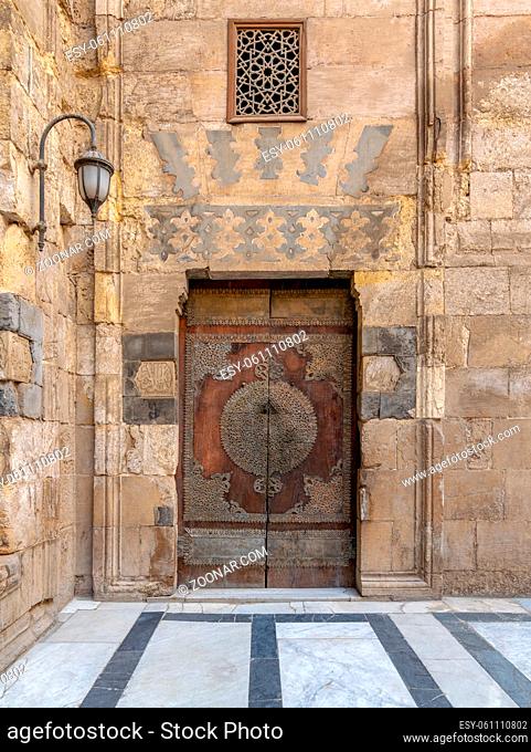 Wooden decorated copper plated door and stone bricks wall at the courtyard of Al-Sultan Al-Zahir Barquq mosque, Al-Moez Street, Old Cairo, Egypt