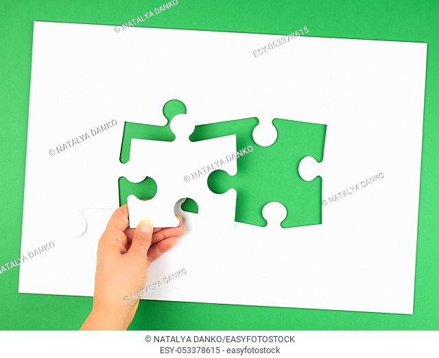 female hand puts empty white big puzzles on a green background, top view