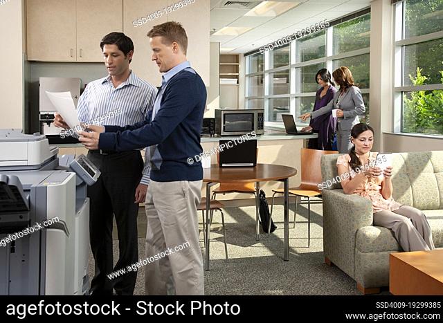 Two coworkers talking at printer while in breakroom at office