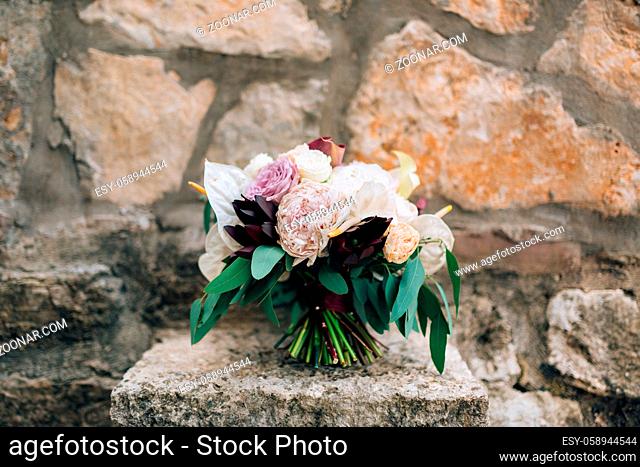 bridal bouquet of white and pink peonies, roses, branches of eucalyptus tree, calla lilies and decorative artichoke on the stone. High quality photo
