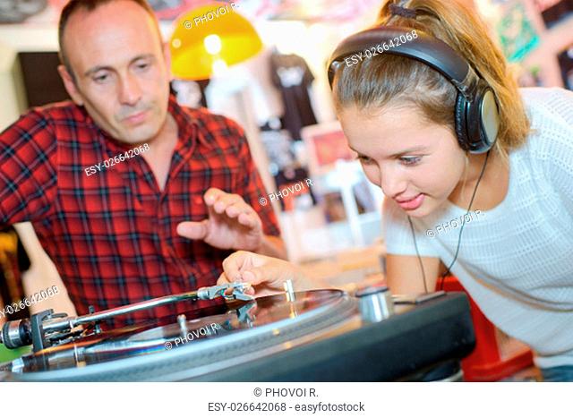 Young lady putting stylus onto record, man urging caution