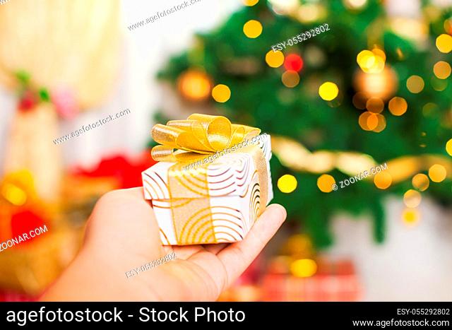 Christmas present in the hand over blurred defocused lights of Christmas tree. Background for design, holiday concept