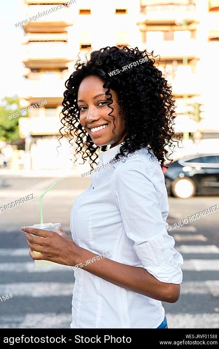 Smiling businesswoman holding juice while standing on road