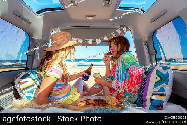 Two girls sitting in a van views to the beach, enjoy food, drinks and relax have a good time