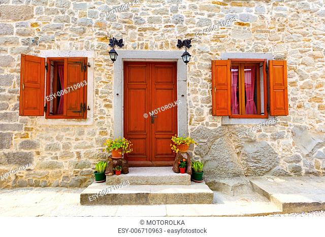house with wooden windows and doors, surrounded in the stone wall. with flowers at the door